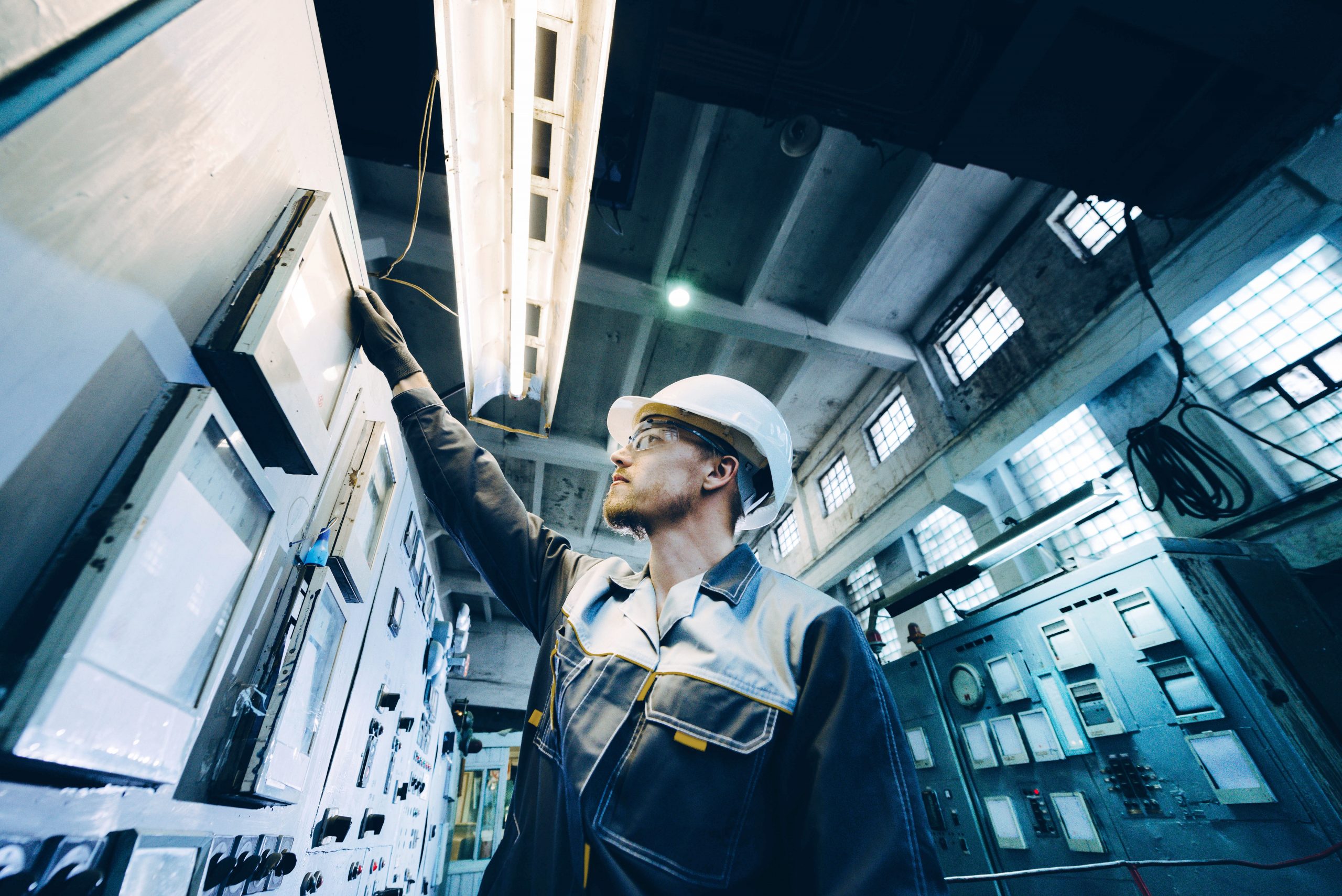 Engineer in a hard hat conducting maintenance on control panel equipment inside a power plant.