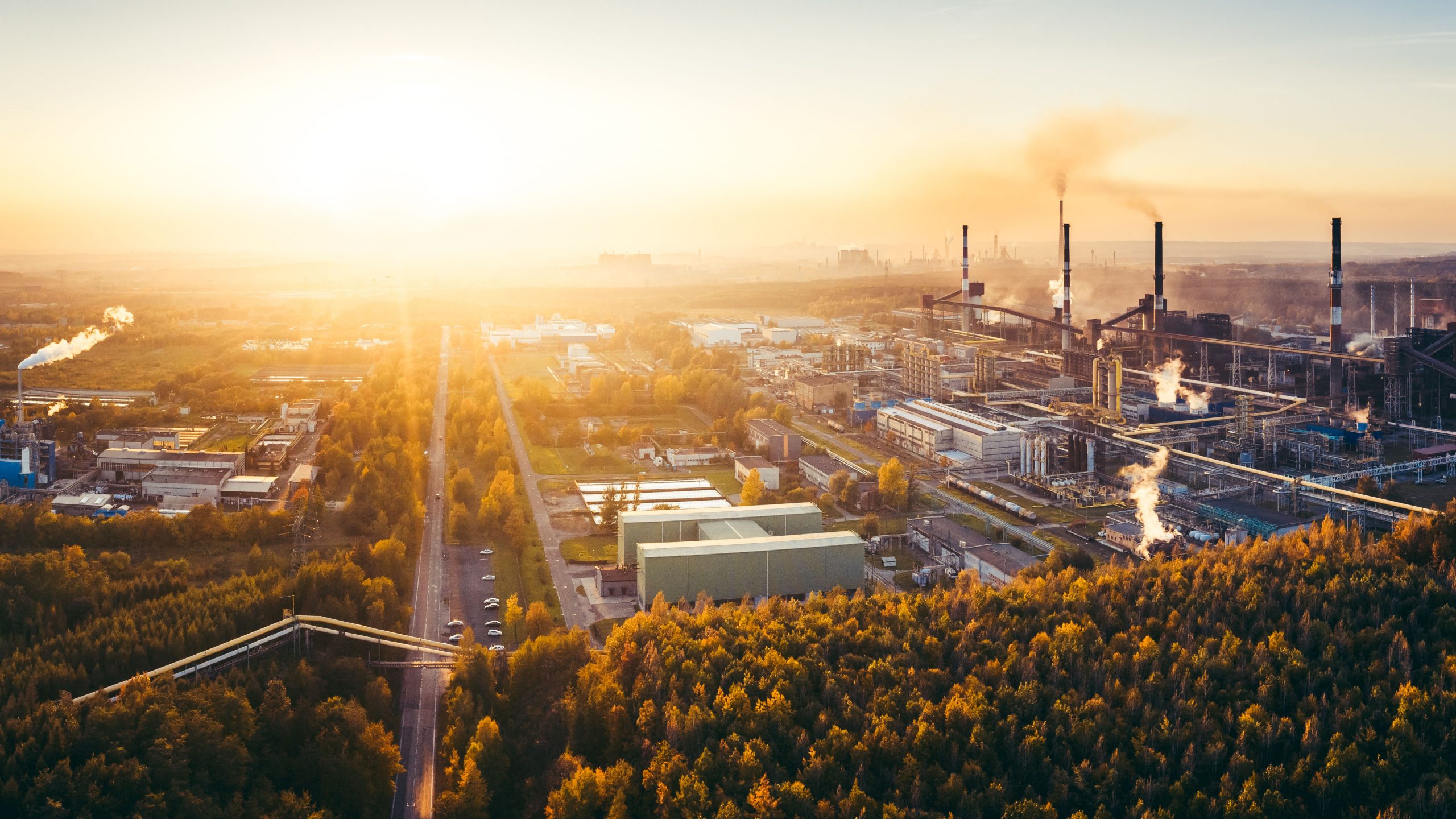 Aerial view of an industrial complex at sunset with emissions visible, highlighting the need for MET's Multi-Stage Humidification CDS-FGD technology for cleaner air.